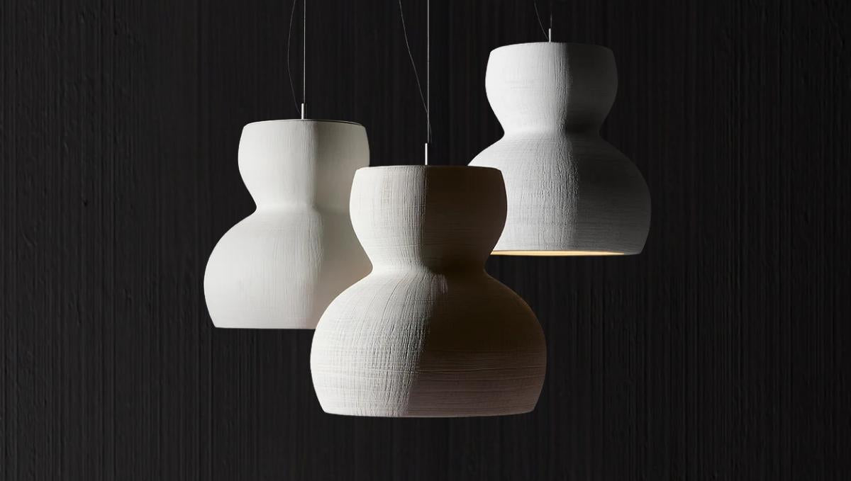 Artisan Lighting Company presents three white pendant lamps gracefully hanging against a black wall.