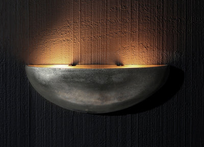 Modern Italian half-moon wall sconce in metallic finish, casting warm indirect light against textured walls.