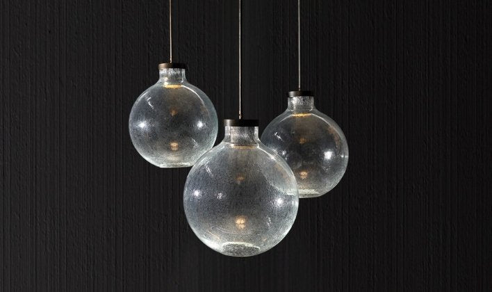 Three glass bottles dangle from a black ceiling, highlighting the craftsmanship of Artisan Lighting Company.